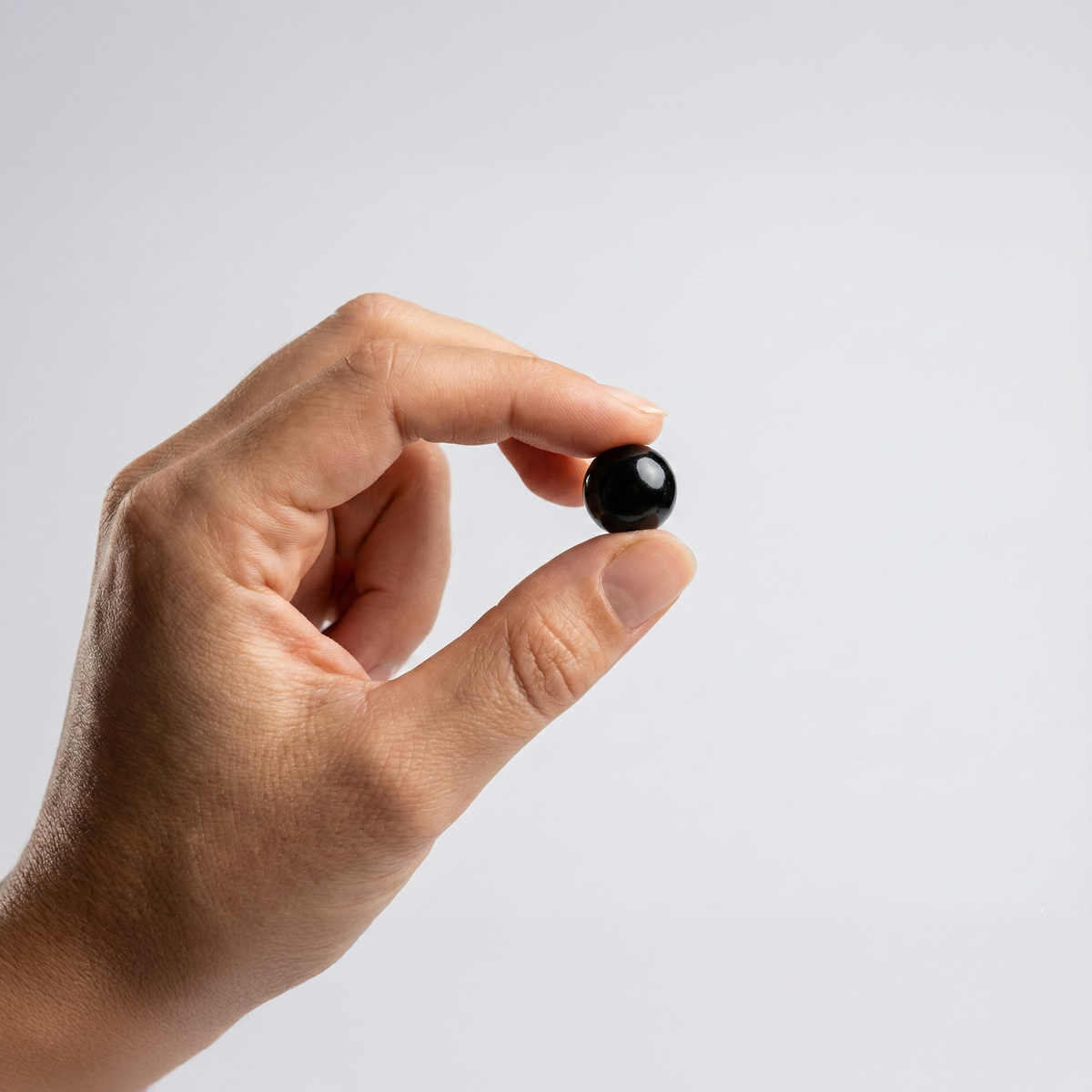 A hand holding single black softgel